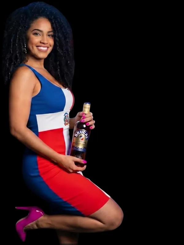 Anfitriona de La Bichota con vestido de la bandera dominicana y una botella de Brugal